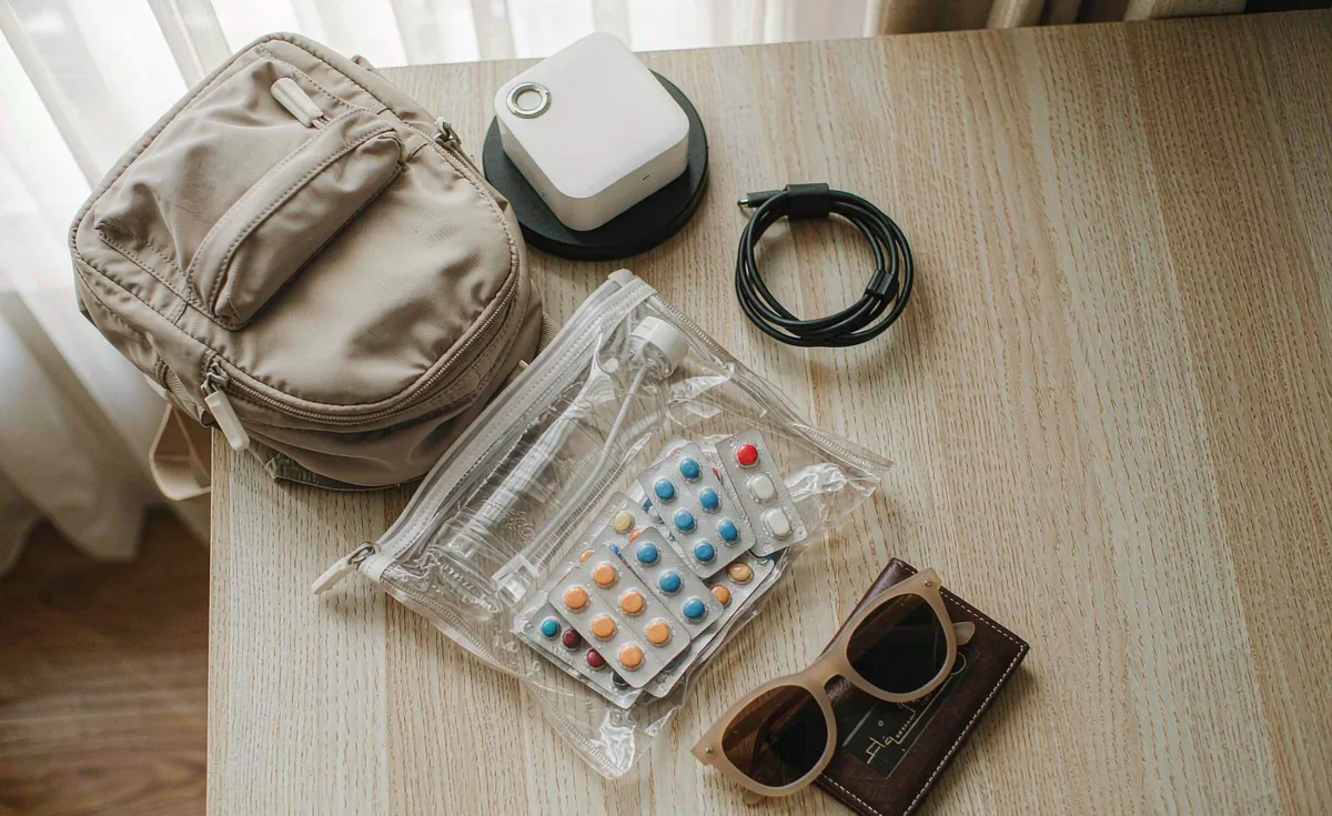 木桌上的出行物品摆拍：小背包、充电宝、数据线、装常用药的透明袋、墨镜和卡包